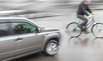 A car about to strike a pedestrian riding a bicycle 