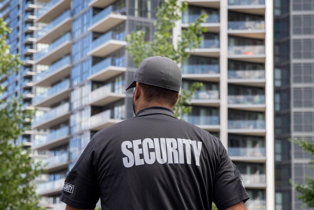 Security guard with his back to the camera, standing in front of a large modern skyscraper.